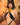Momokun wearing a black strappy outfit, cat ears and gold jewelry against a brick wall