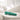Turquoise handheld massager on a white surface with a blurred background