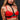 Woman wearing a red bra with gold chains and black harness against a dark background