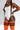 A model wearing a white bodysuit paired with bright orange ribbed knee-high socks featuring black stripes, shown against a light gray studio background.