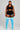 A plus-size model stands against a light gray studio background wearing a black sports bra and shorts with white trim, paired with bright blue over-the-knee socks featuring white stripes near the top.