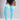 A model wearing bright light blue ribbed over-the-knee socks with white horizontal stripes near the top, paired with a black bodysuit against a light gray studio background.
