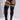 Black cable-knit over-the-knee socks with three horizontal striped bands in orange, yellow, and teal, shown on a model wearing a black bodysuit against a light gray studio background.