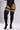 Black cable-knit over-the-knee socks with three horizontal striped bands in orange, yellow, and teal, shown on a model wearing a black bodysuit against a light gray studio background.