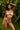 Woman in a light pink lingerie set standing in a lush green outdoor setting