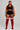 A plus-size model stands against a light gray studio background wearing a black sports bra and shorts with white side stripes, paired with red over-the-knee socks featuring white horizontal stripes near the top.