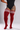 A model wearing red ribbed over-the-knee socks with three white stripes at the top, paired with a black bodysuit, shown against a light gray studio background.