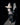 A model wearing a dark costume with padded shell cup, fishtail bones skirt with glitter tulle layers, and gloves, posed with one hand on her head