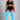 A woman modeling a black sports bra and matching black athletic shorts with white side stripes, paired with bright turquoise ribbed over-the-knee socks, against a solid gray studio background.