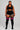 A woman modeling a black athletic set consisting of a sports bra, high-waisted shorts with white piping, and black thigh-high socks with pink stripes, against a light gray studio background.