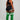 A woman stands in profile wearing a black sports bra and shorts with white side stripes, paired with bright green over-the-knee socks featuring white horizontal stripes near the top. She is photographed against a plain light gray studio background.