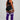 A woman stands in profile wearing a black sports bra and shorts with white side stripes, paired with purple over-the-knee socks featuring white horizontal stripes near the top.