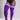 A model wearing bright purple ribbed over-the-knee socks with white athletic stripes near the top, paired with a black bodysuit against a light gray studio background.