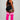 A woman stands in profile against a light gray studio background, wearing a black athletic crop top and shorts with white trim, paired with bright pink over-the-knee socks featuring three white horizontal stripes near the top.