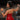Woman in a red dress with leather straps and cuffs, wearing a collar, in a dimly lit room.