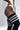 A close-up of a model's hip and upper leg wearing navy blue ribbed thigh-high socks with white stripes, paired with a white bodysuit. The model has a large black tribal-style tattoo on her upper thigh.