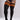 Black ribbed thigh-high socks with three orange stripes near the top, shown on a model wearing a black bodysuit against a light gray studio background.