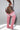 Pink over-the-knee socks with white stripes at the top, worn by a model with a large thigh tattoo, in a studio setting.