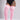 A model wearing pink ribbed over-the-knee socks with white stripes near the top, paired with a black bodysuit against a light gray studio background.