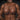 Man wearing brown silicone breasts against a dark brick wall