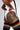 A close-up lifestyle shot of a model wearing a white bodysuit, black ribbed thigh-high socks with rainbow stripes, and a large black tattoo on her upper thigh, set against a plain light gray background.