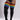 A person modeling black ribbed over-the-knee socks with bold rainbow stripes near the top, shown against a light gray studio background.