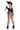 A woman modeling a revealing black and brown harlequin-patterned costume with matching garter belt, fishnet stockings, black boots, and a small black hat, posed against a plain white background while holding a knife prop.
