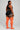 Person wearing black athletic top and shorts with orange knee-high socks on a gray background