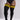 A model wearing black ribbed thigh-high socks with bold yellow and black horizontal stripes near the top, paired with a black bodysuit against a light gray studio background.