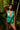Woman wearing a green and blue tropical print romper standing in a tropical setting with palm leaves.